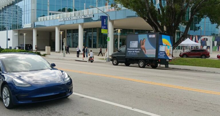 Discover Card Spanish ad on digital billboard truck near Miami Convention Center, with blue car and people passing by