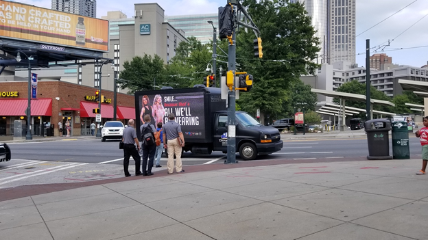 Mobile billboard advertising promoting dental services by SMILE modeled by smiling women, stopped at a city intersection.