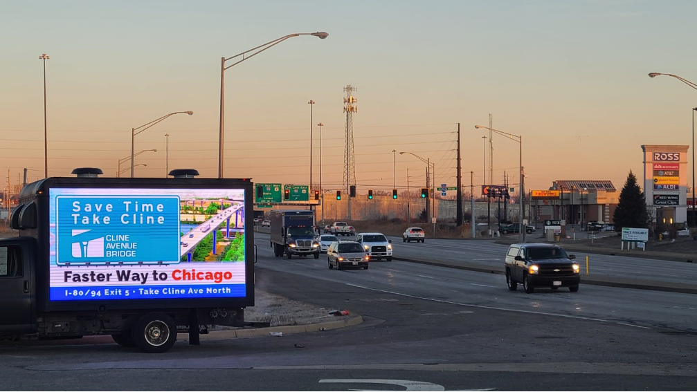Can't Miss US Mobile billboards marketing ad on a road at sunset advertising Cline Avenue Bridge as a faster Chicago route.