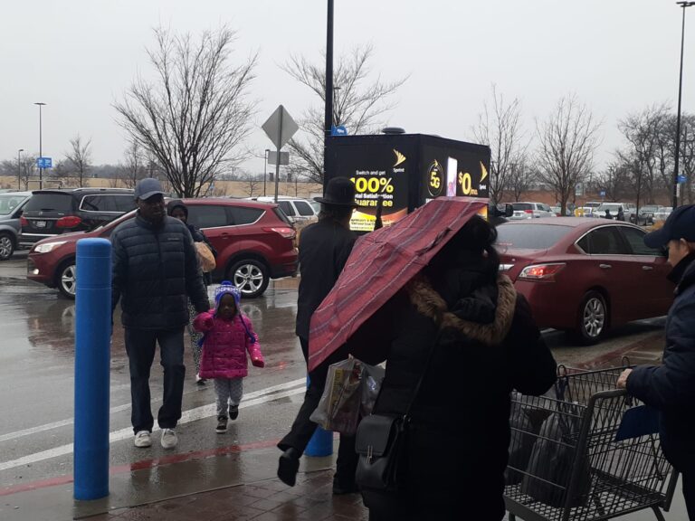 Mobile Billboard Advertisement truck idling in a jampacked parking area with a busy crowd of shoppers on a rainy weather - Mobile LED billboard trucks