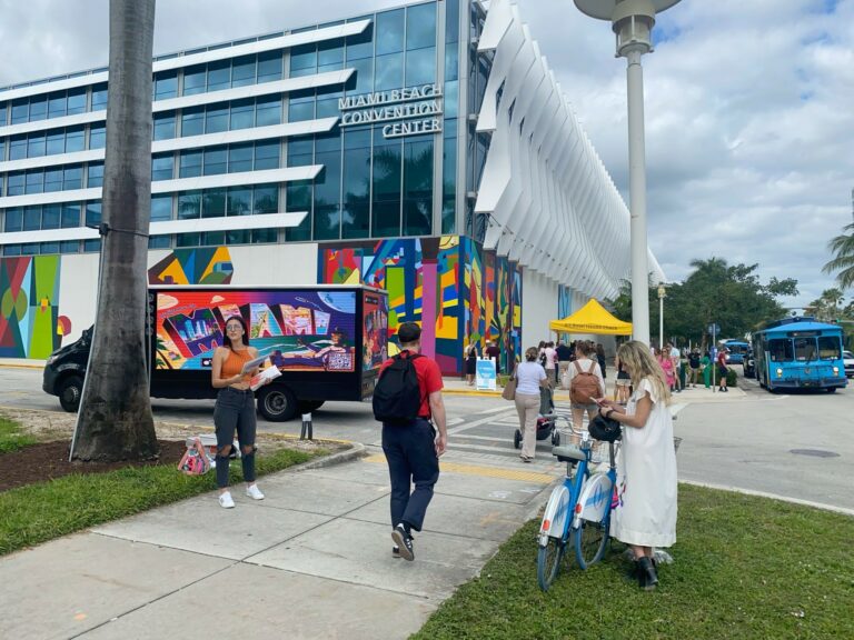 Mobile Billboard placed in front of the Miami Convention Center. People walking close. LED billboard truck shows Miami Ad in vibrant colors.