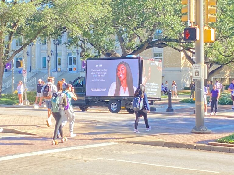 Students grabbing attention ad by Cantmiss.US Mobile Billboards promoting local hair styling services at a bustling intersection.