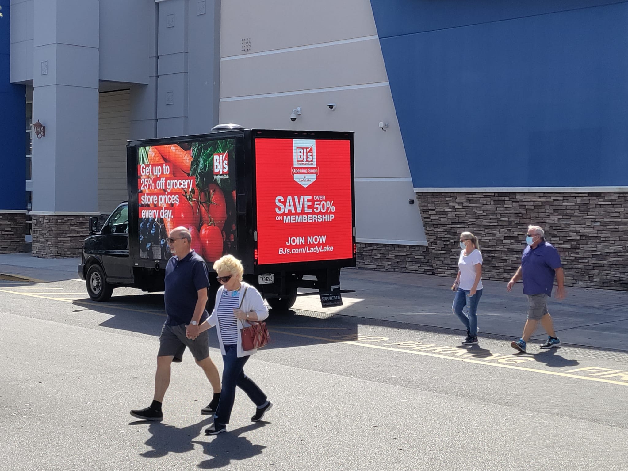 Mobile Billboard parked near store with people walking by. Ad shows red screen with strawberry
