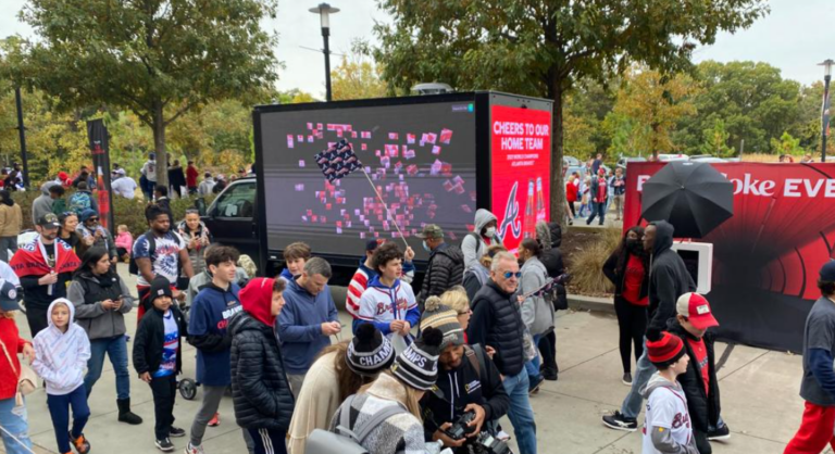 A lively gathering in Georgia with diverse groups of people, a large screen showcasing an animated U.S. map, and a promotional booth celebrating the home team with the "A" logo.