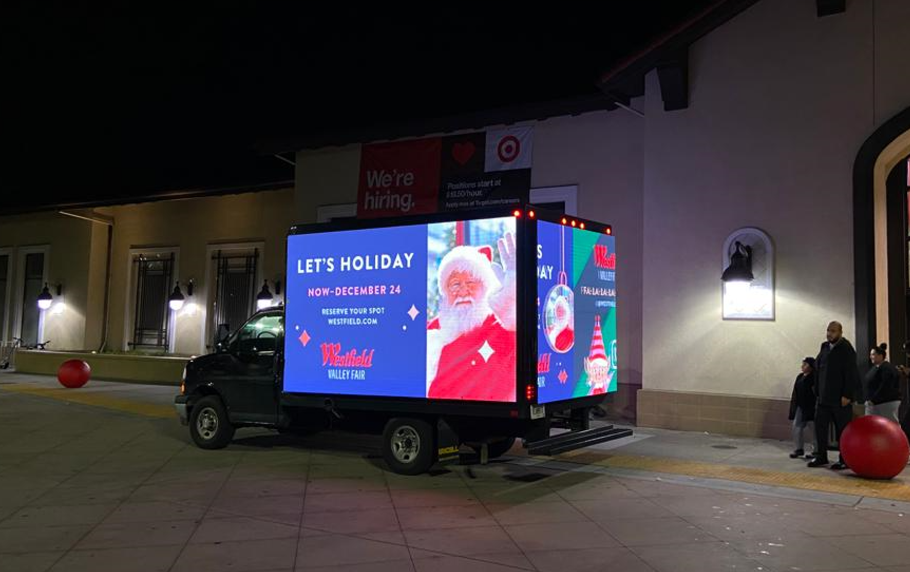 A Cantmiss.US digital mobile billboard truck showcasing holiday advertisements by Westfield Valley Fair, parked near a bustling shopping area in the evening.