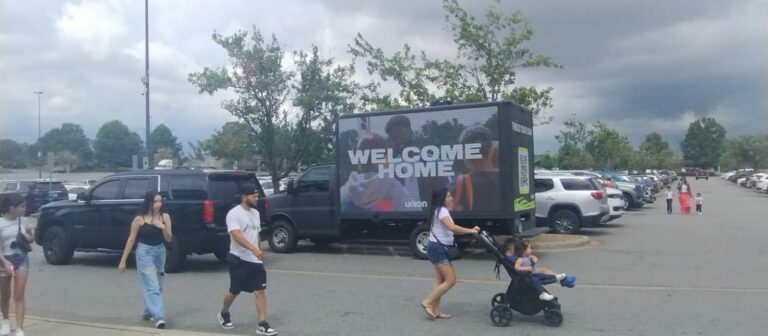 Cantmiss.US' Digital Billboard Truck in a parking lot displaying a 'WELCOME HOME' advertisement by Union Church, amid a crowd.
