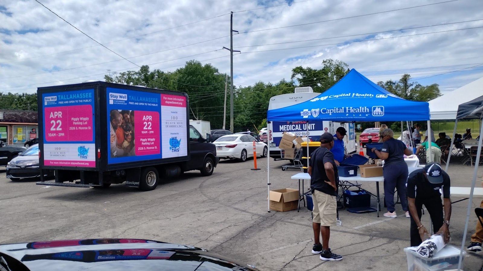 Digital billboard truck parked near a blue outdoor tent where Capital Health is having an outdoor clinic. People working around the tent