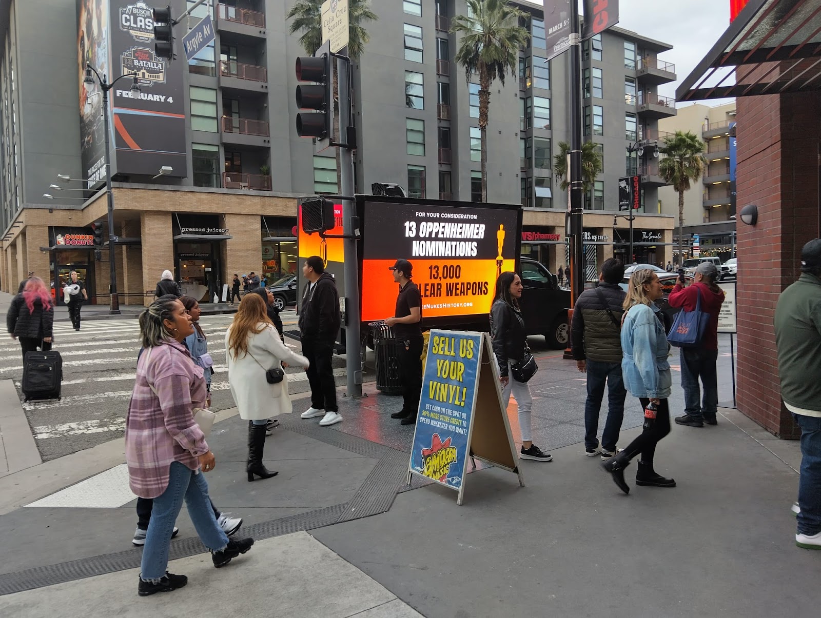 Pedestrians by led advertising truck. LED truck parked near sidewalk and black and orange color with Oppenheimer and weapons.
