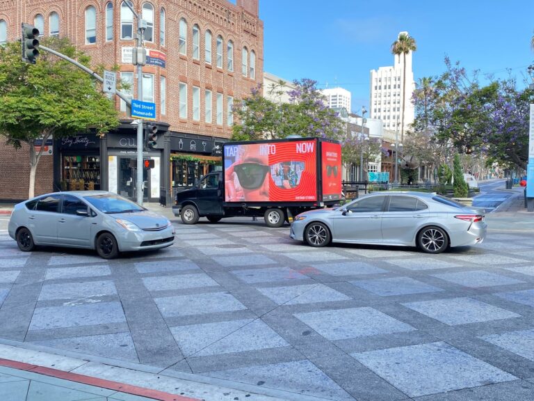 A Mobile Billboards in Los Angeles, advertising Rayban featuring their new Glasses with camera in a white and red contrast with other cars.