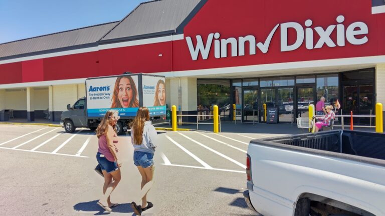 Aaron's rent-to-own Mobile billboard truck advertisement parked outside Winn-Dixie Supermarket in bright daylight with shoppers passing by