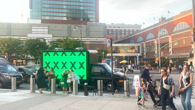 Outdoor advertising truck for Ed Sheeran's concert promotion parked across Stop & Shop Pharmacy with several people taking a picture beside it.