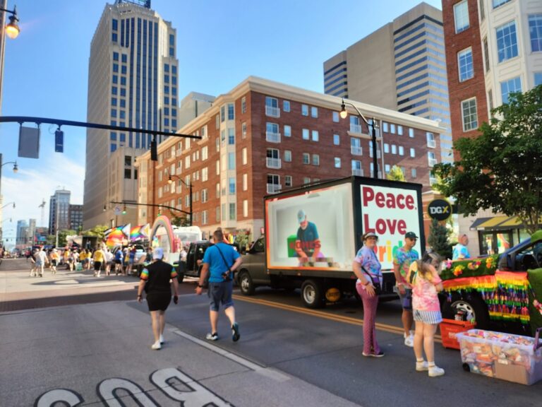 Mobile LED truck at a street event promoting Peace, Love, Pride. Several people are seen to be celebrating "Pride Month".